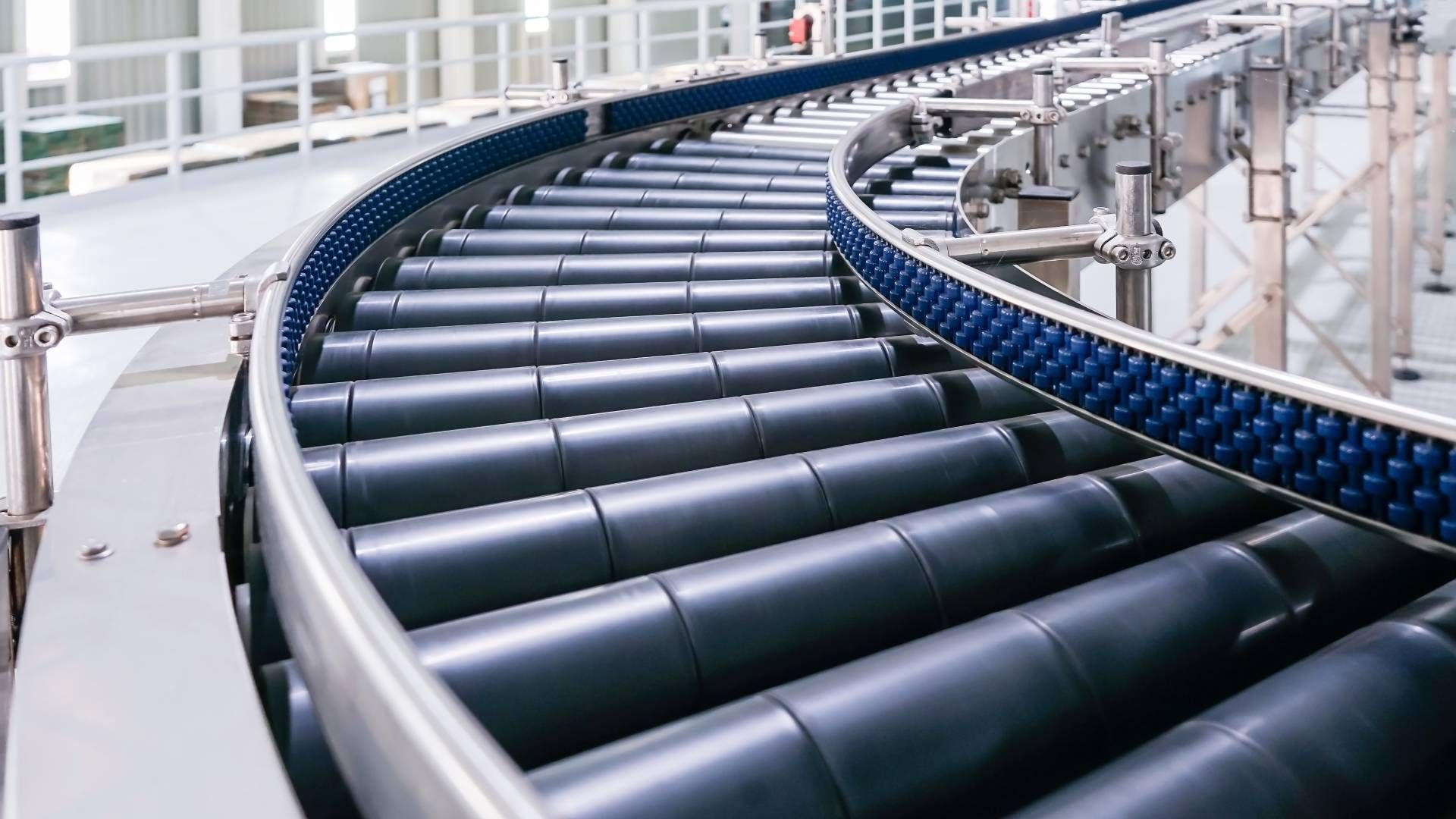 Curved conveyor belt with black rollers, blue side rails, in a factory setting.