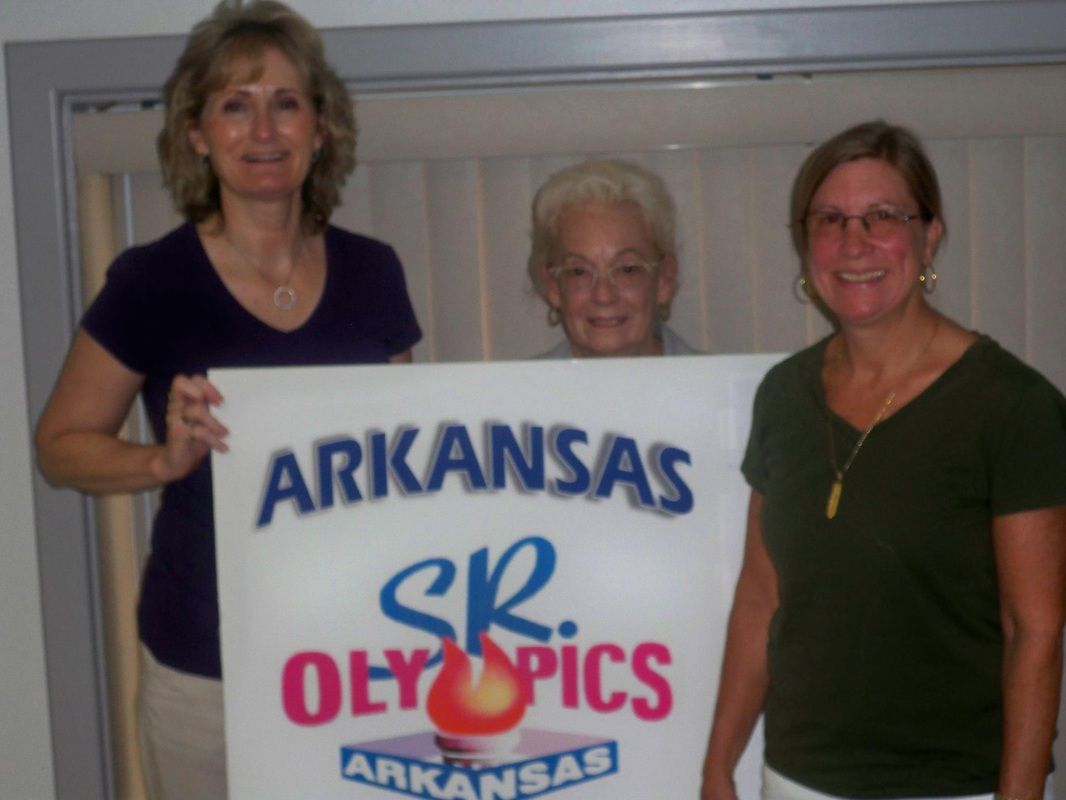 Three women holding a sign that says arkansas sr olympics