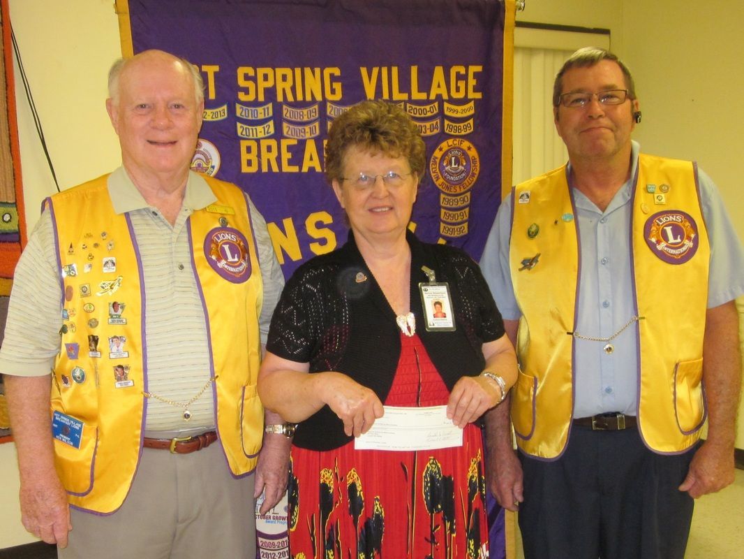 Two men and a woman standing in front of a spring village banner