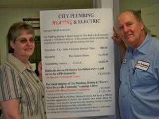 A man and a woman are standing next to a sign that says city plumbing heating & electric.