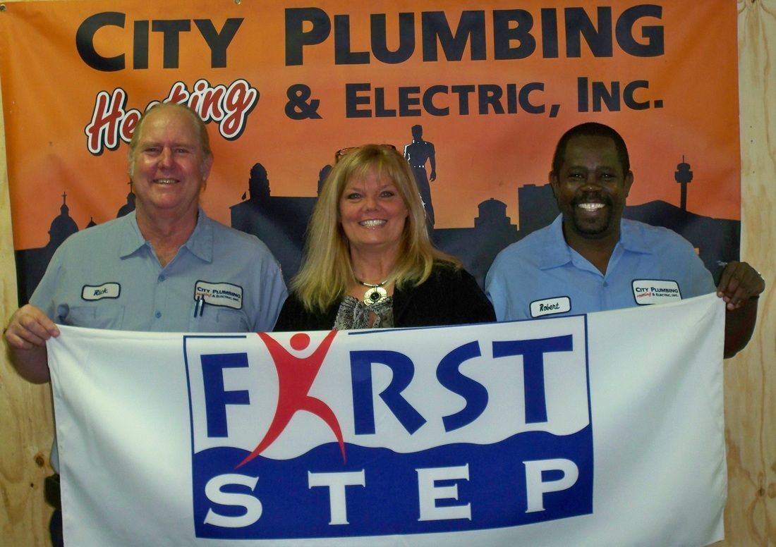 Three people holding a first step banner in front of a city plumbing and electric inc. banner