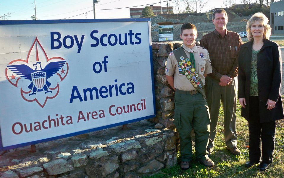 A boy scout stands in front of a boy scouts of america sign