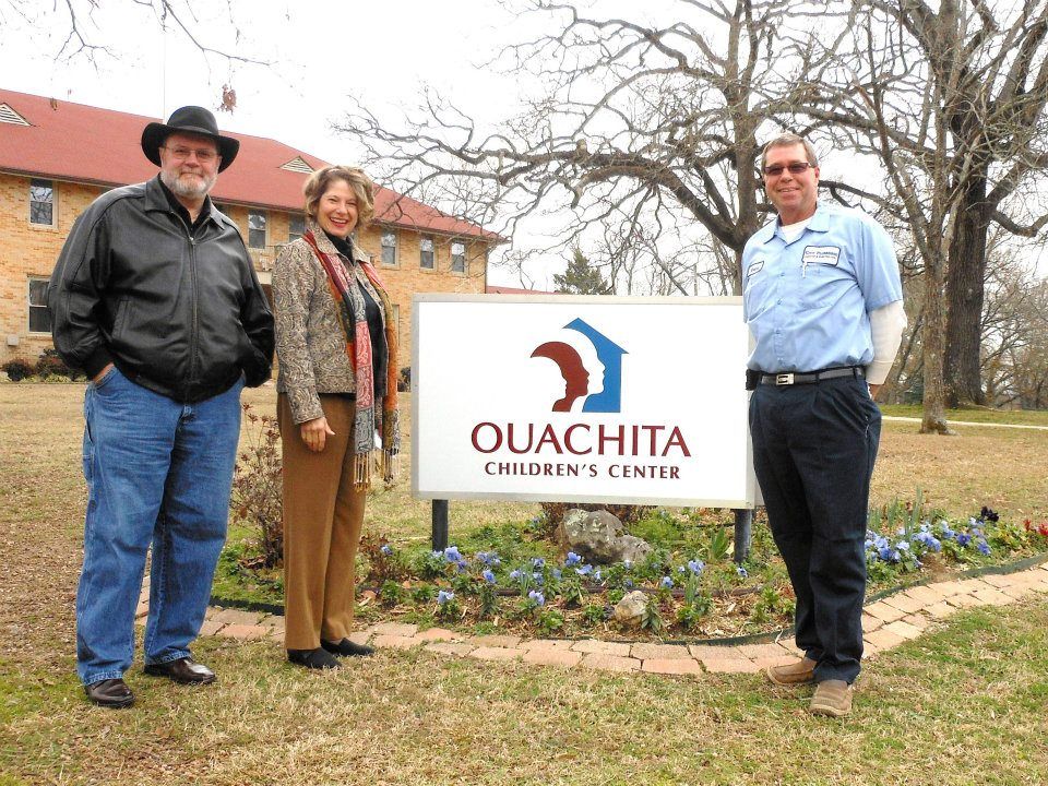 Three people standing in front of a ouachita children 's center sign