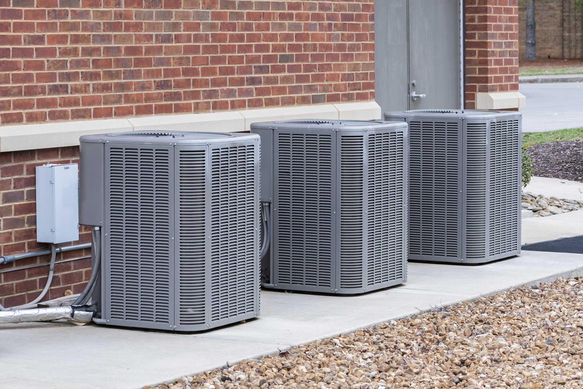 Three air conditioners are sitting outside of a brick building.