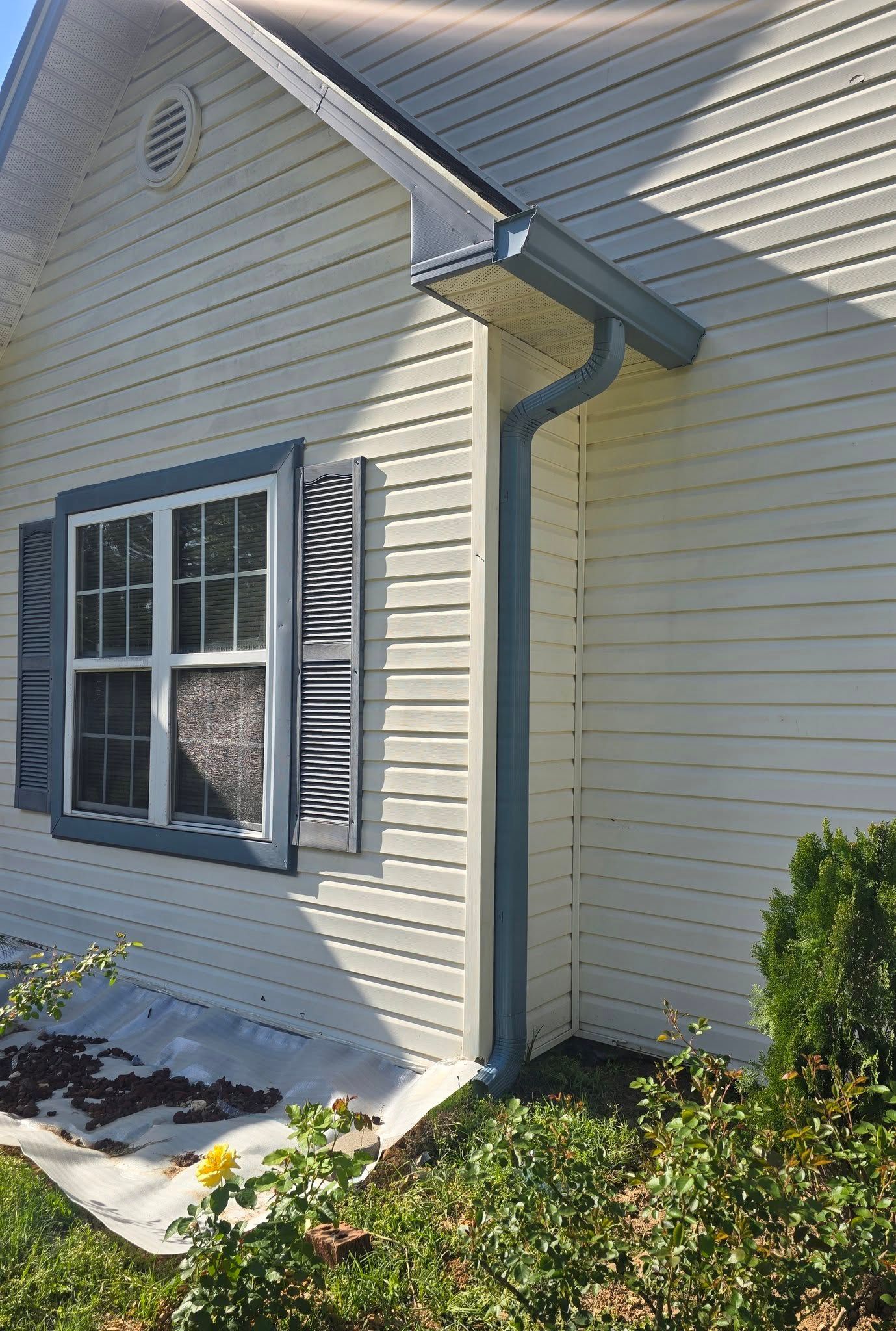 A side view of a cream-colored house with dark grey window shutters, trim, and a matching gutter downspout.