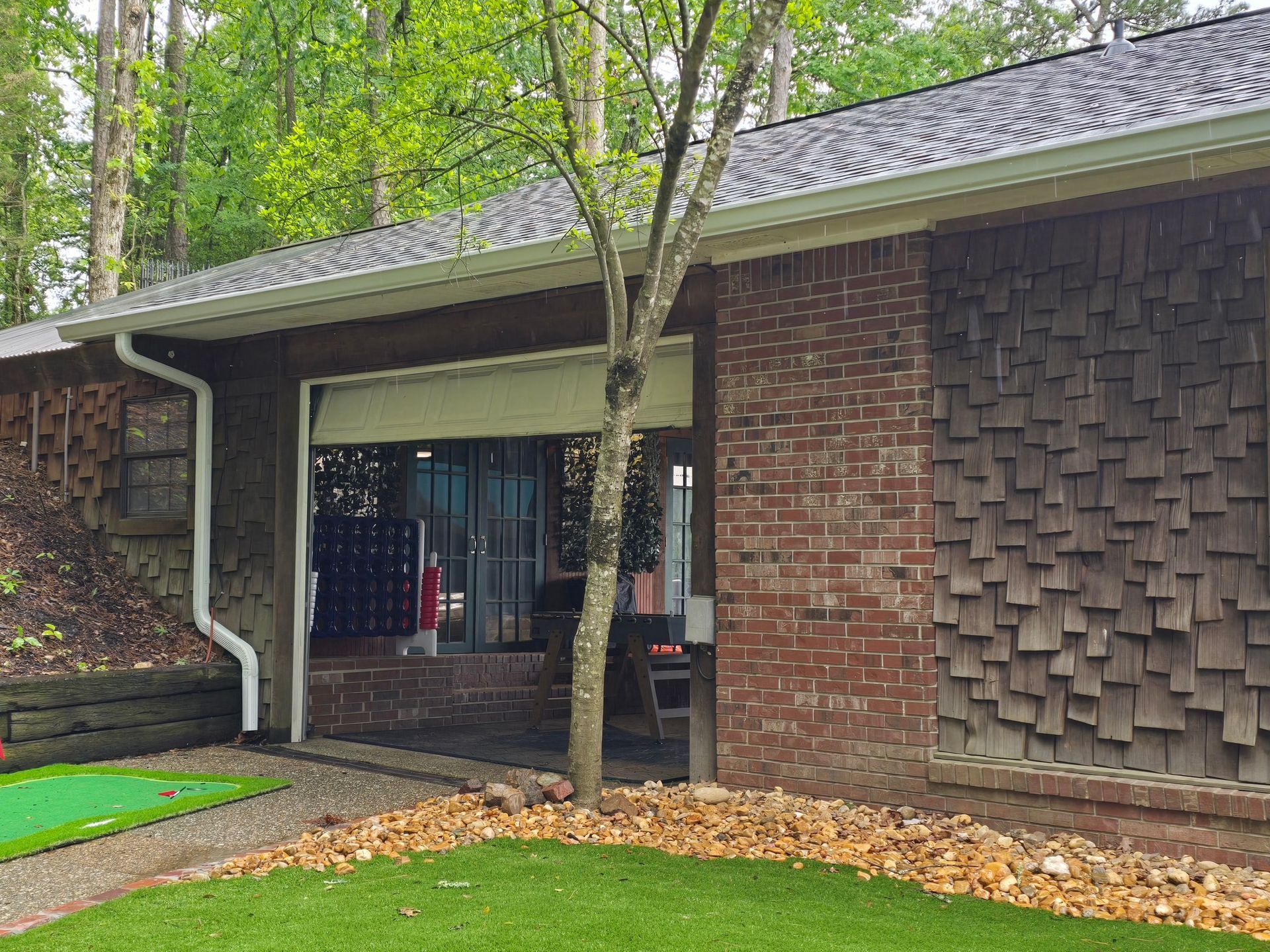 A side view of a cream-colored house with dark grey window shutters, trim, and a matching gutter downspout.