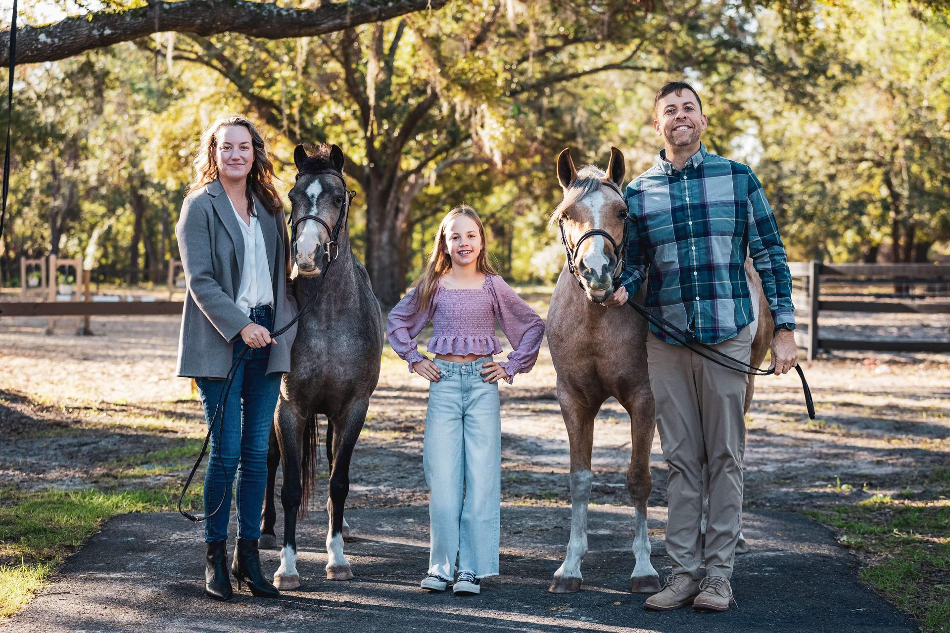 Family posing with two horses on a path in an outdoor setting.