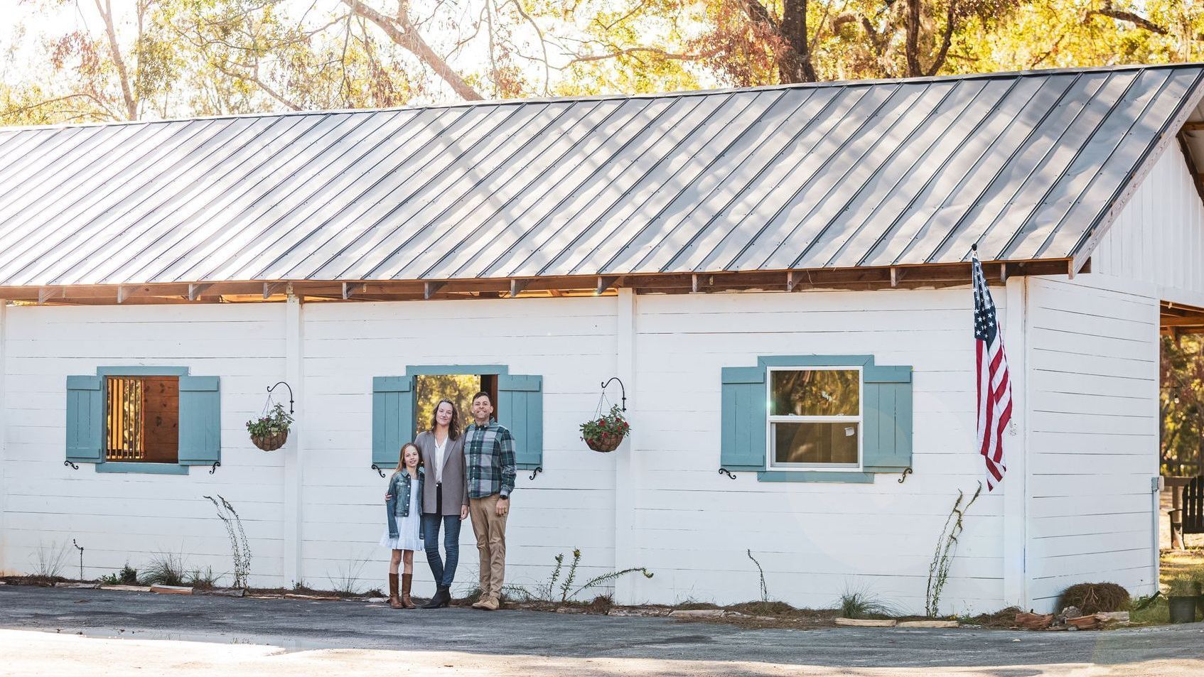 Family standing in front of a white building with blue shutters and an American flag.