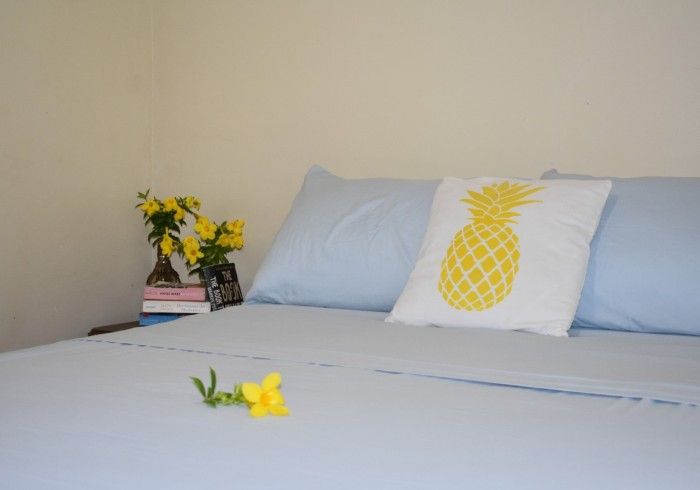 Light blue bed with pineapple pillow, yellow flowers, and a small yellow flower on the blanket