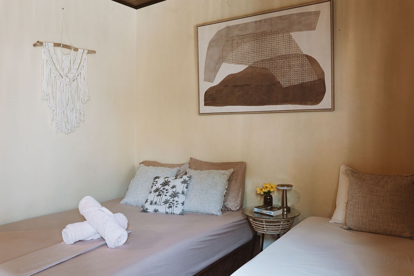 Cozy bedroom with two beds, beige walls, framed art, and folded towels on the left bed.