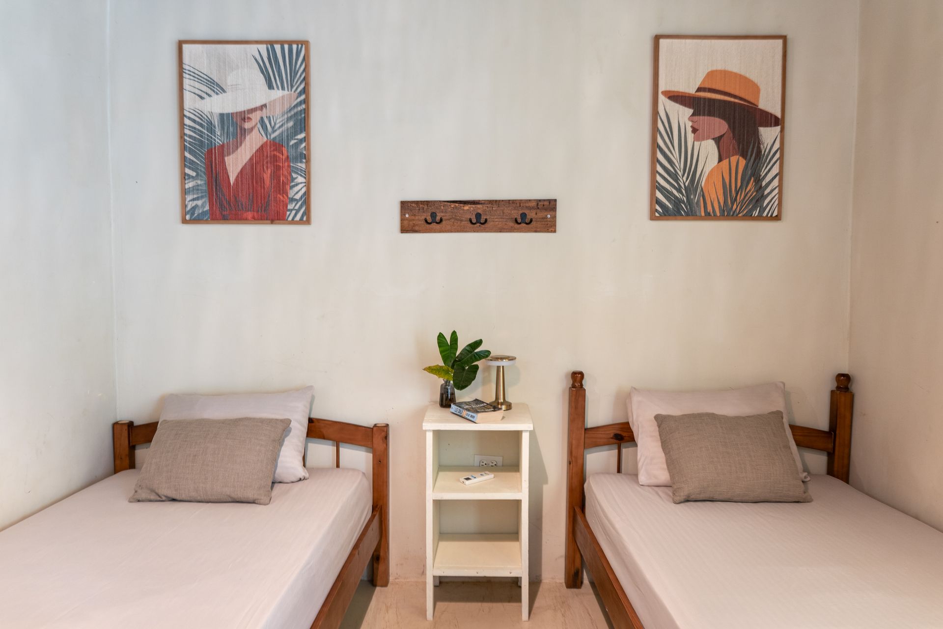 Two twin beds in a minimalist room with wall art and a small nightstand between them