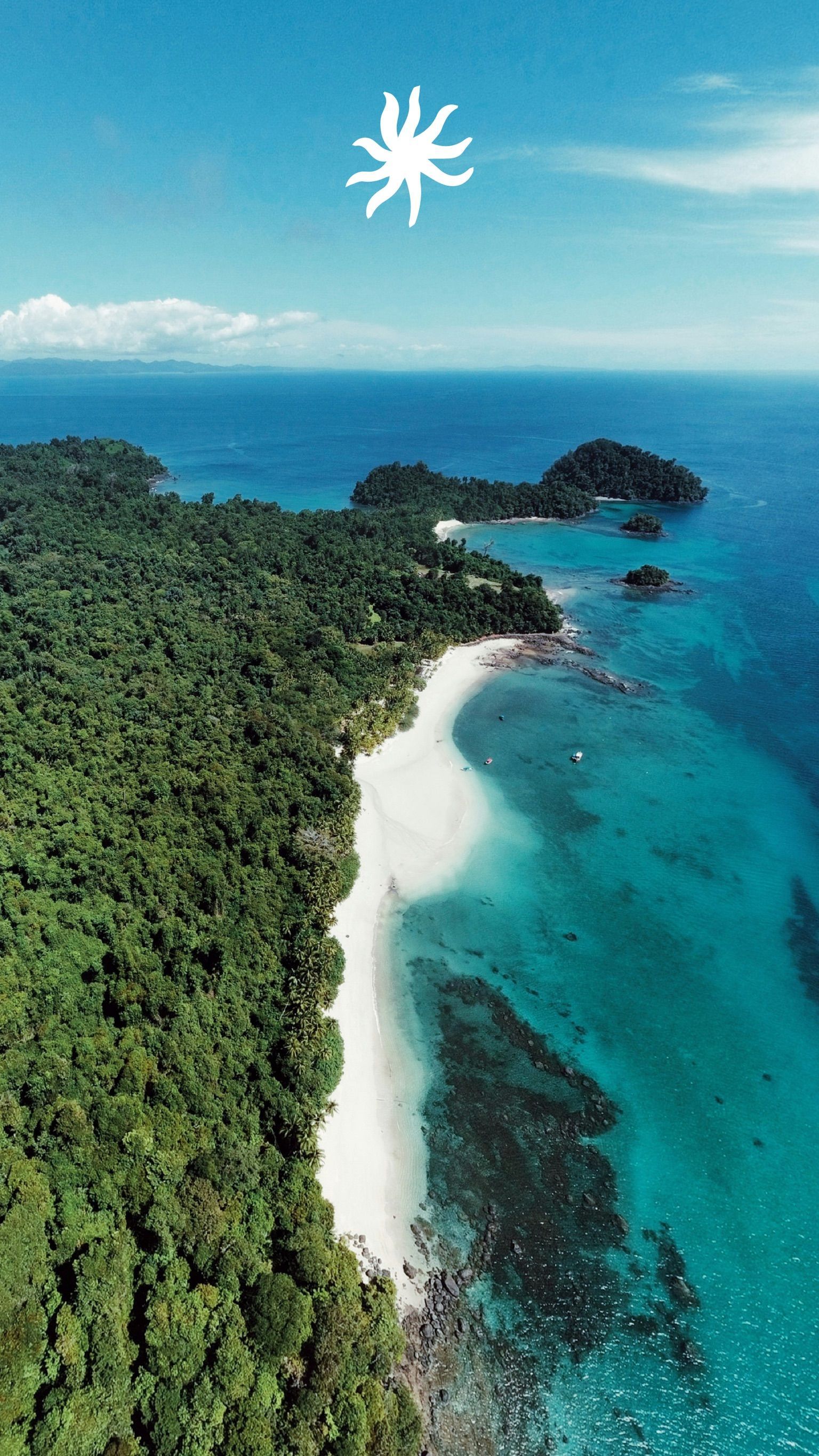 Aerial view of a tropical island with white sandy beach, turquoise water, and dense green जंगल.