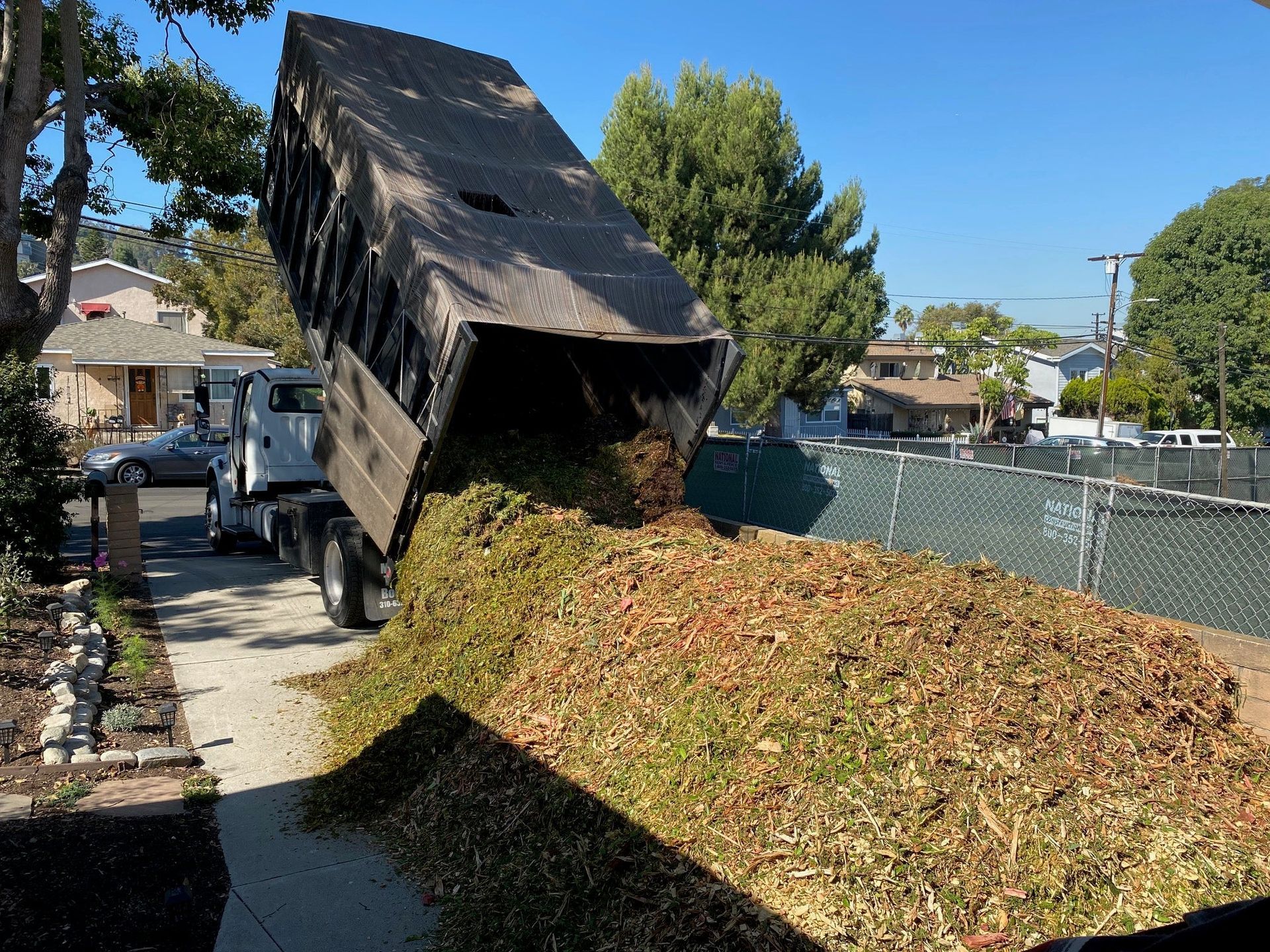 A dump truck is dumping a pile of leaves on the side of the road.