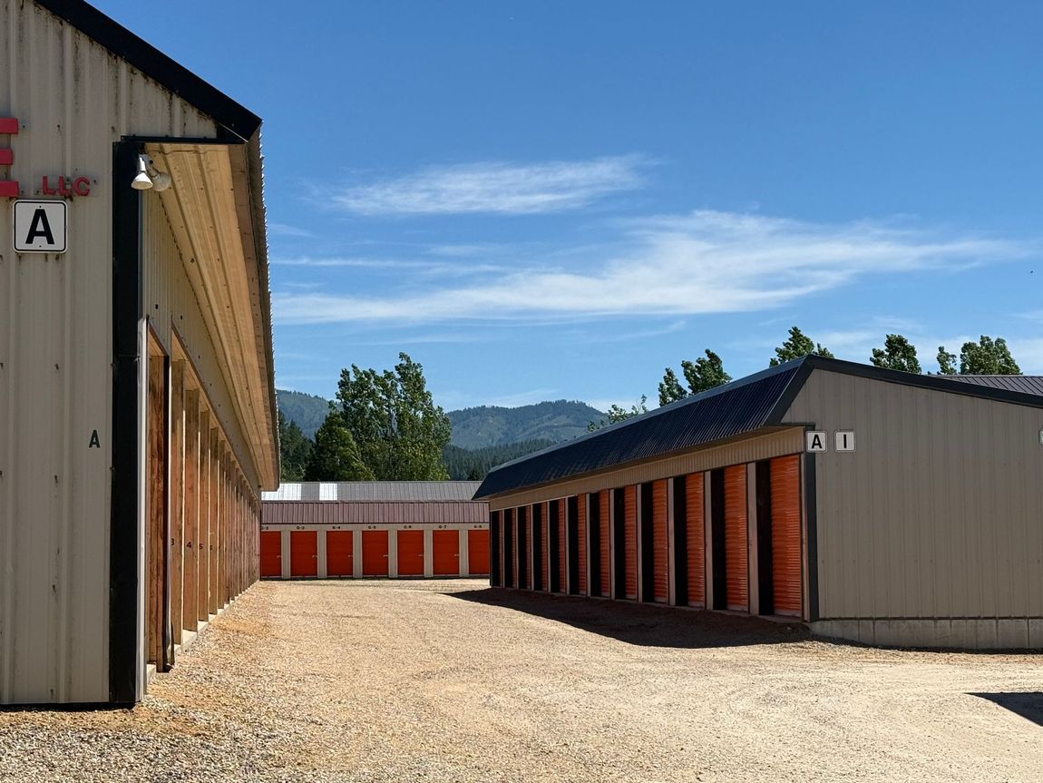 Row of storage units with open bays and gravel lot under a blue sky, mountains in the distance