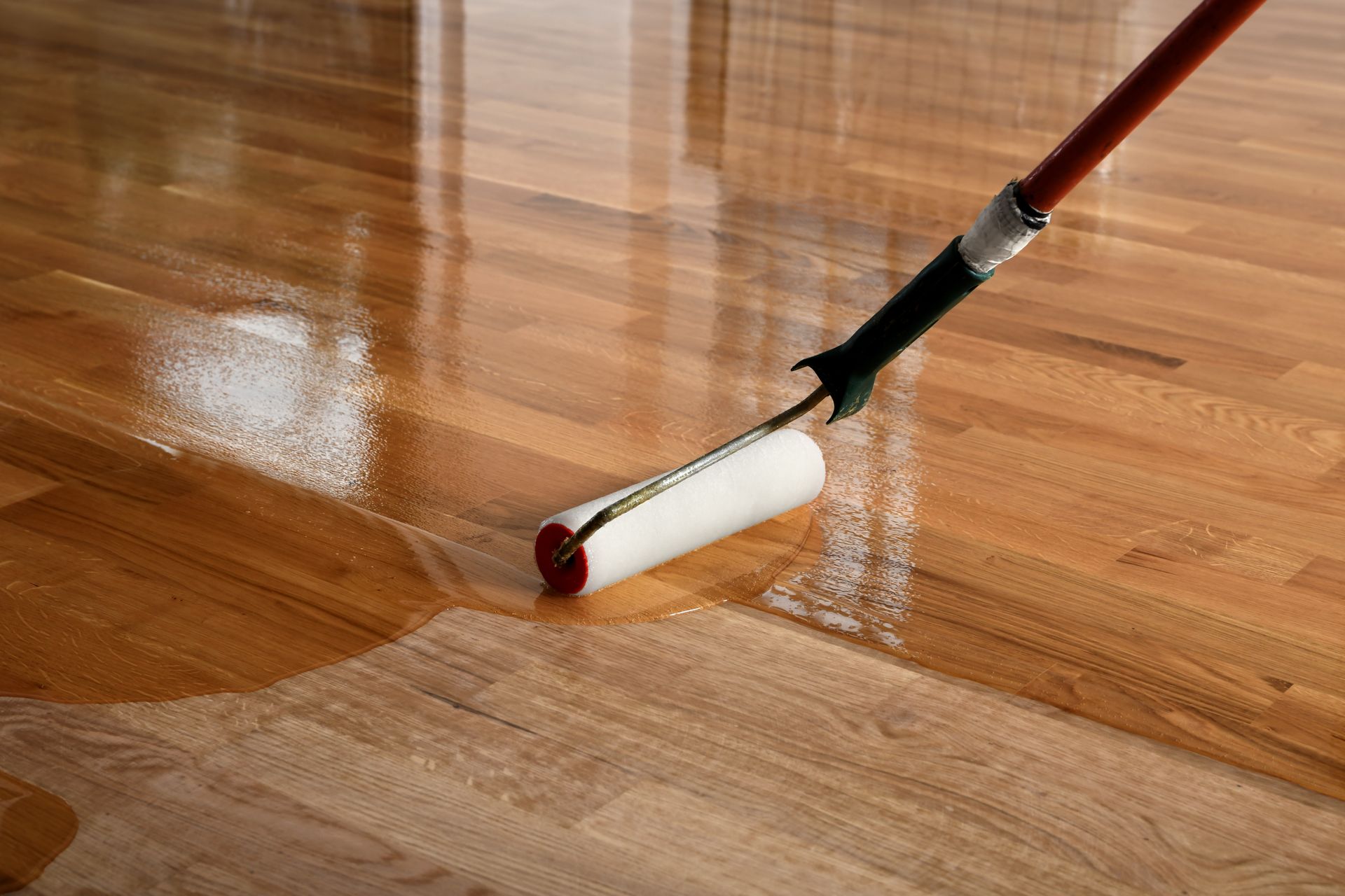 A person is painting a wooden floor with a roller.