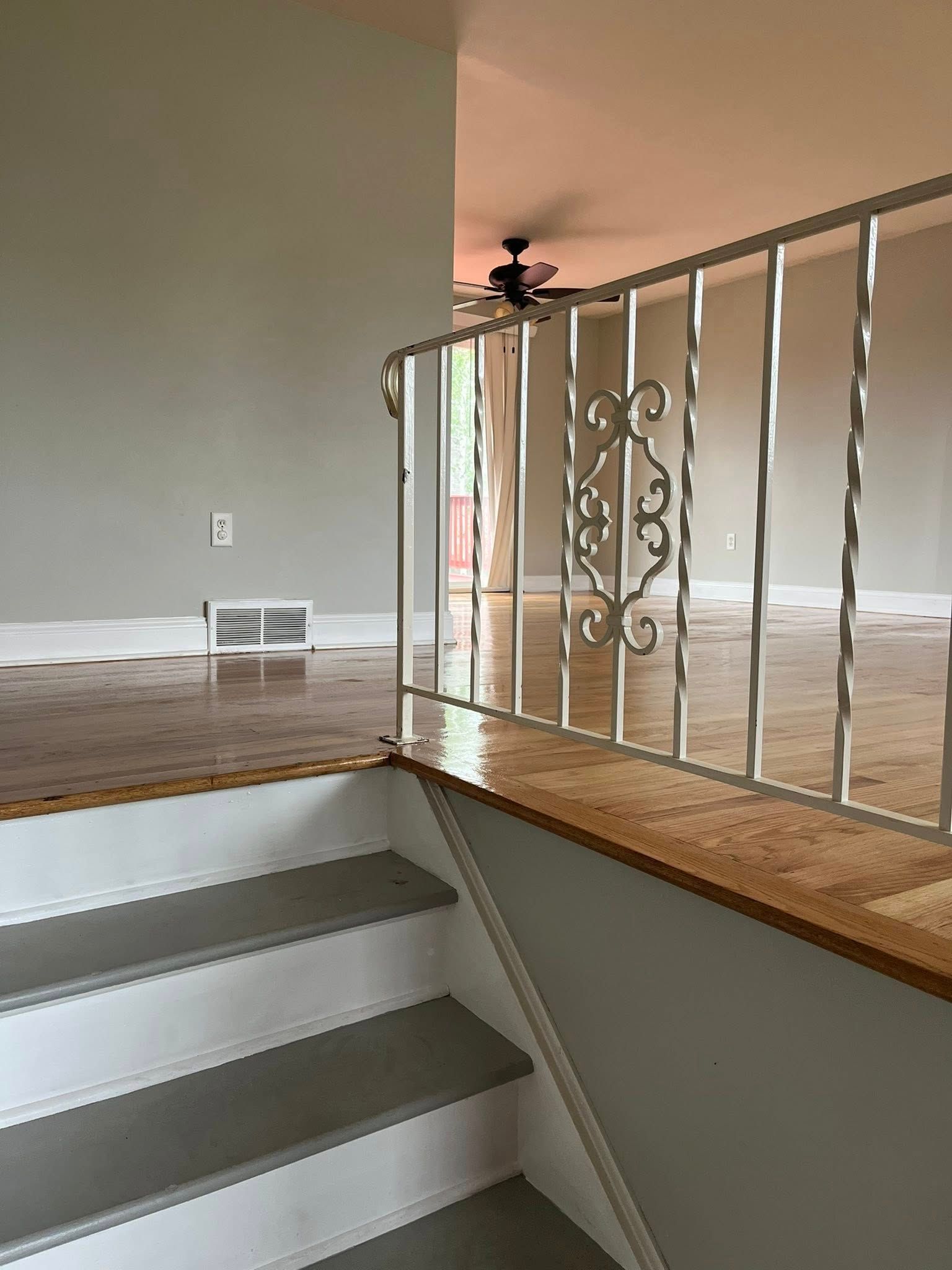 A staircase leading up to a living room with a wrought iron railing and a ceiling fan.
