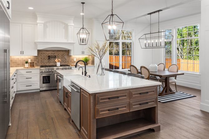 Bright modern kitchen with white cabinets, marble island, pendant lights, and dining area by large windows