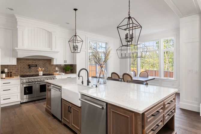 Bright white kitchen with large island, pendant lights, and stainless steel appliances under tall windows