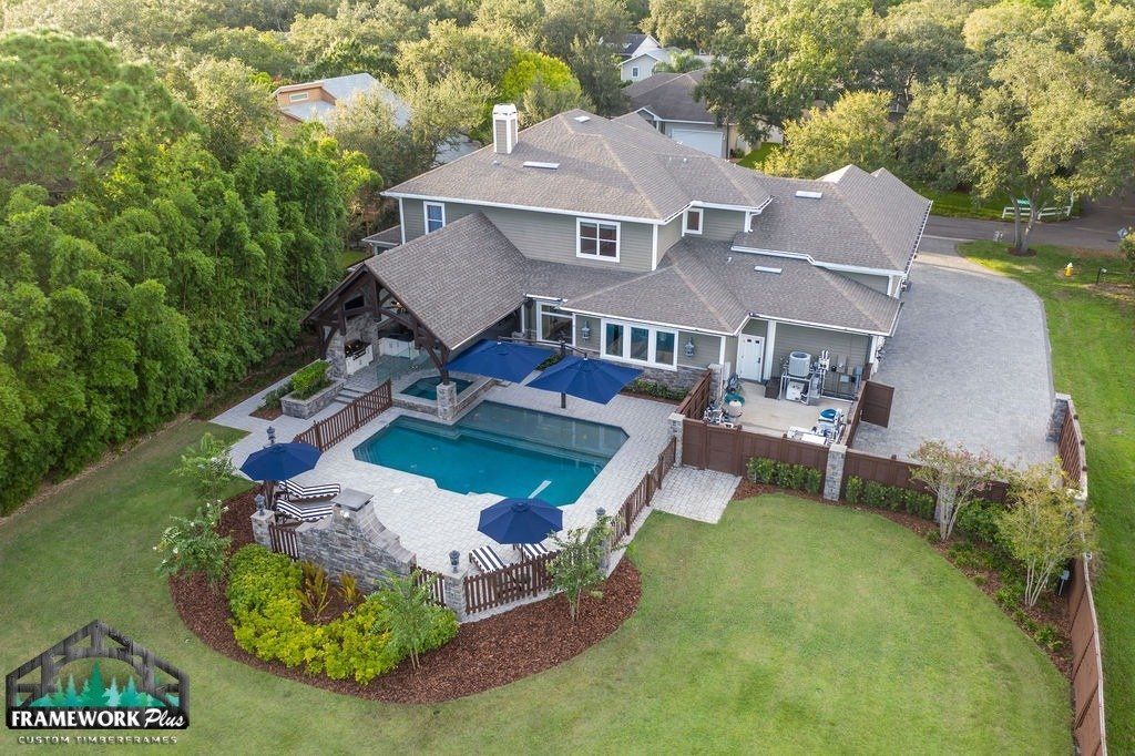 An aerial view of a large house with a large swimming pool surrounded by trees.