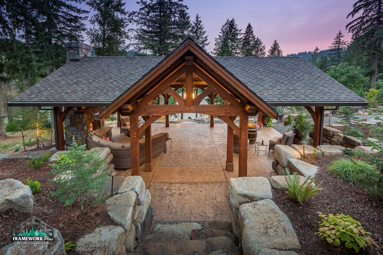A wooden gazebo with a roof is surrounded by rocks and trees.