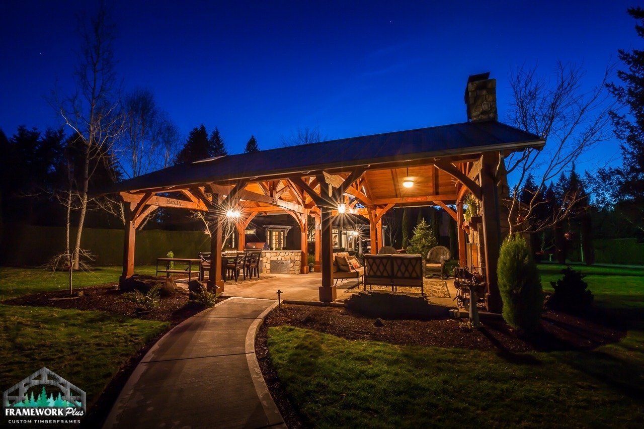 A wooden pavilion is lit up at night in a backyard.