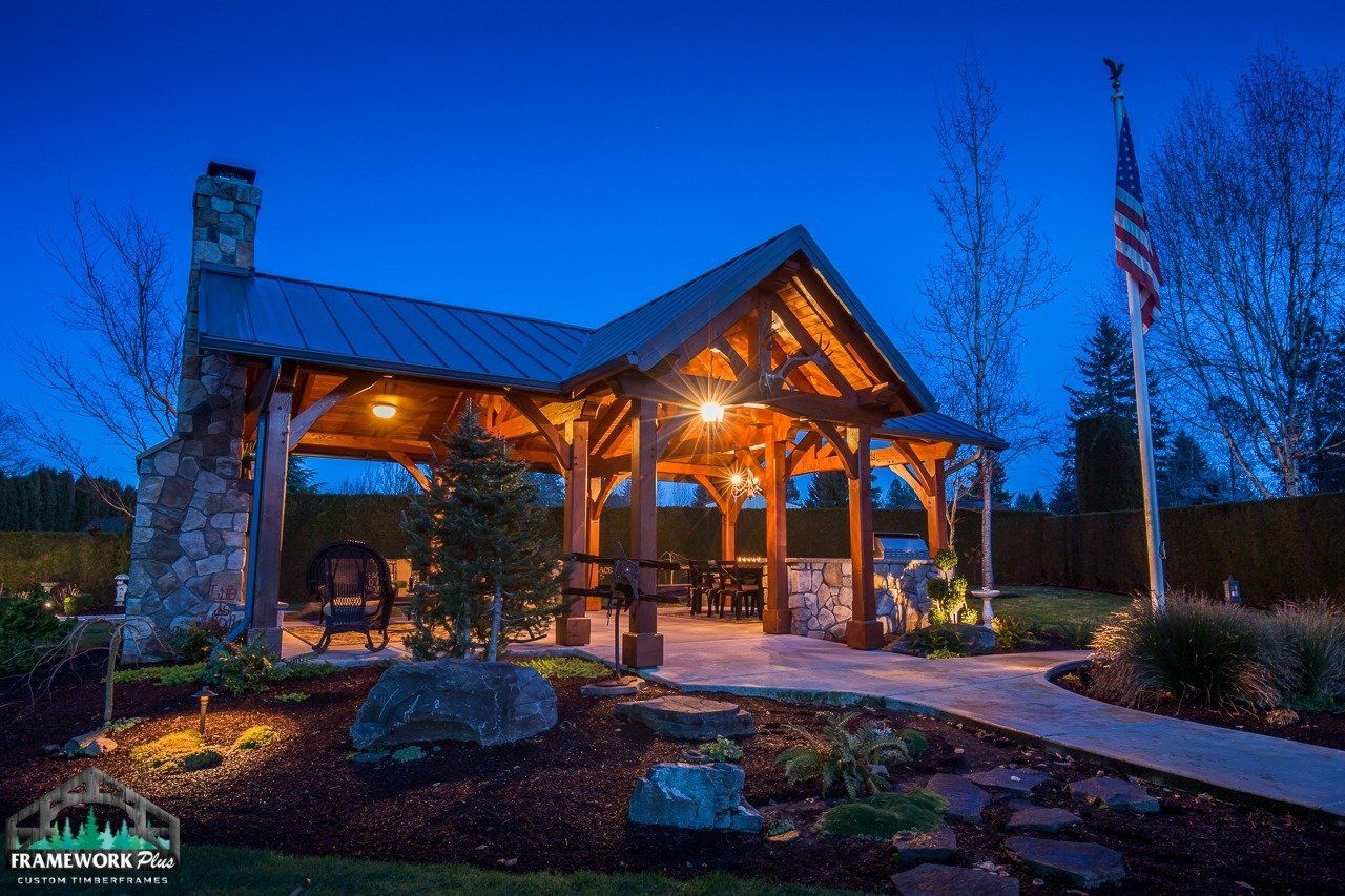 A large wooden pavilion with a metal roof is lit up at night.