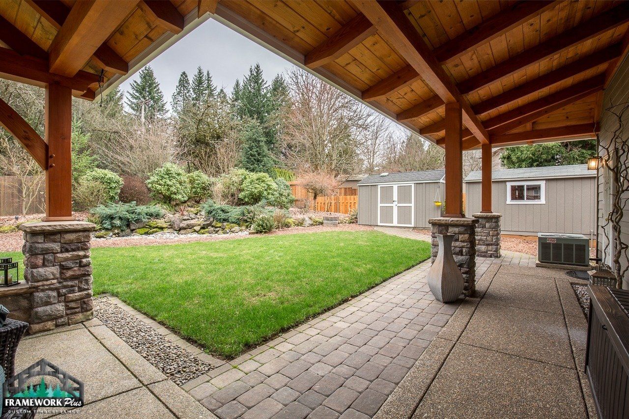 A covered patio with a wooden roof overlooking a lush green yard.