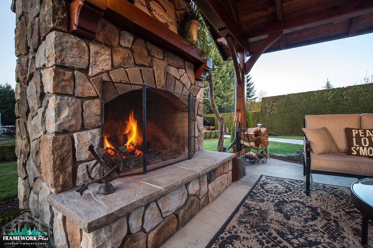 A large stone fireplace is sitting under a covered patio.