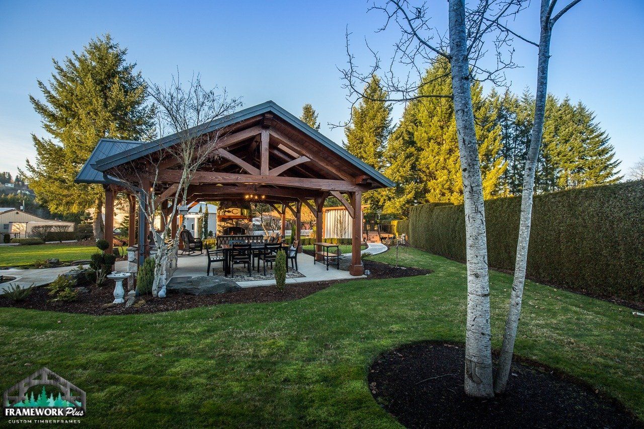 A wooden pavilion with a table and chairs in a backyard surrounded by trees.
