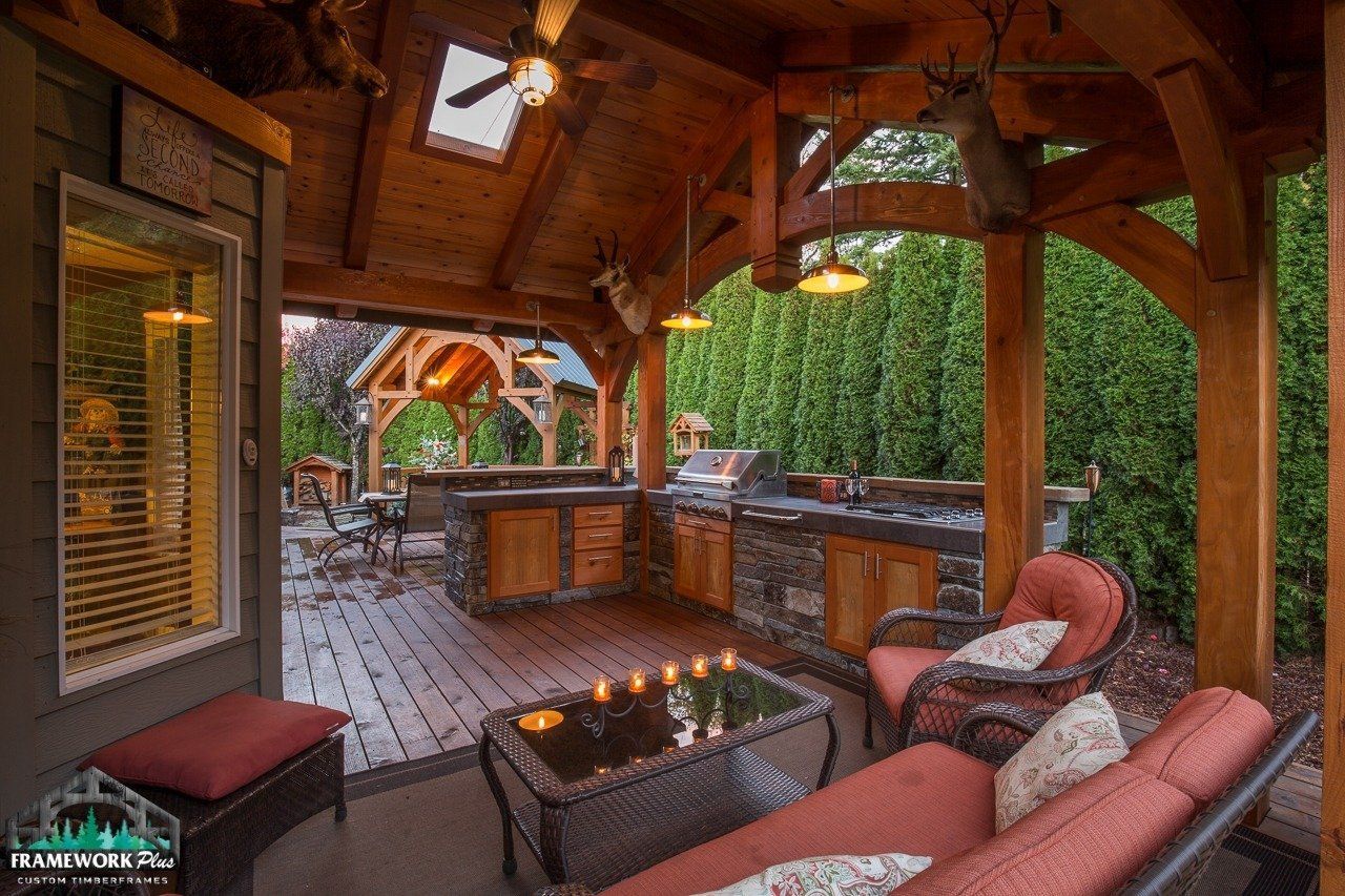 A wooden gazebo with a couch , chairs , and a table.