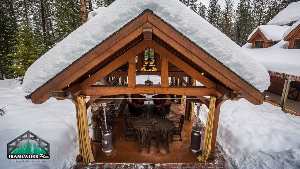 A wooden pavilion covered in snow with a table and chairs underneath it.