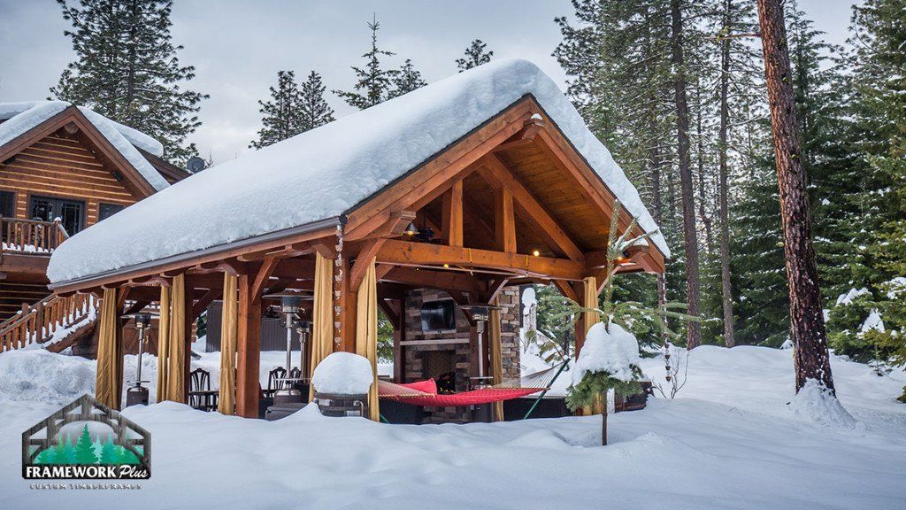 A wooden house with snow on the roof is surrounded by snow covered trees.