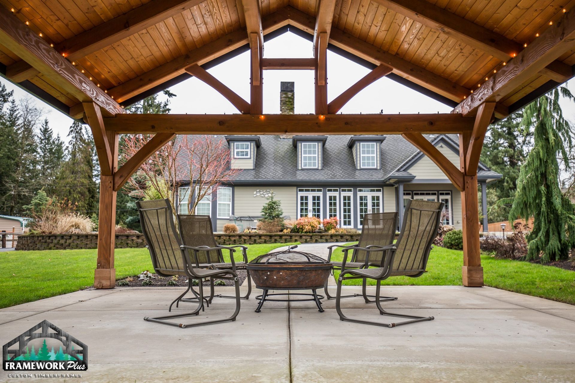 A wooden gazebo with a table and chairs underneath it in front of a house.