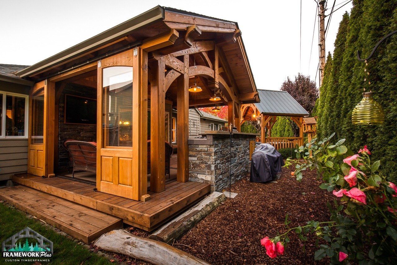 A wooden pavilion with sliding glass doors is sitting in the backyard of a house.