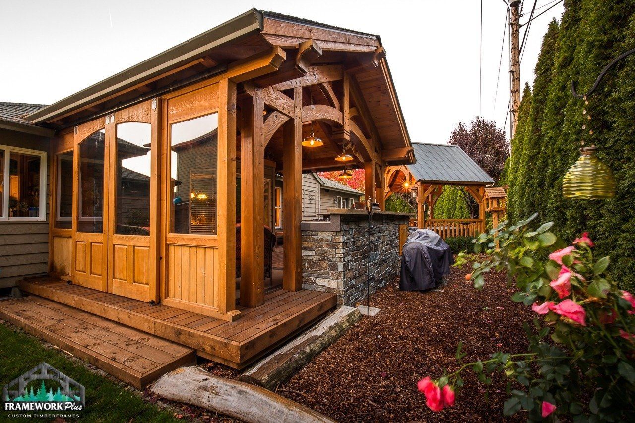 A large wooden structure with a lot of windows is in the backyard of a house.