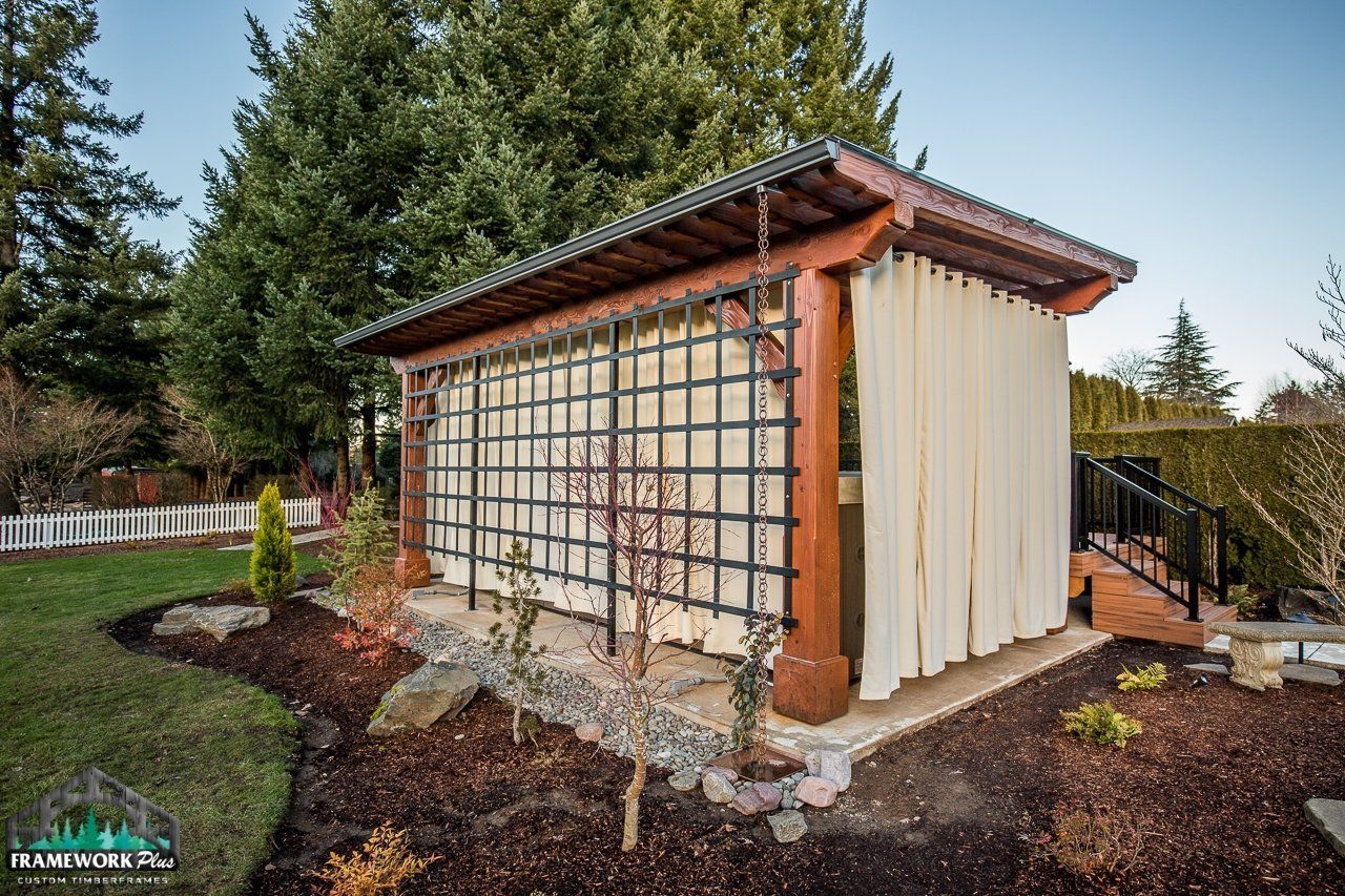 A wooden gazebo with white curtains is in the middle of a garden.