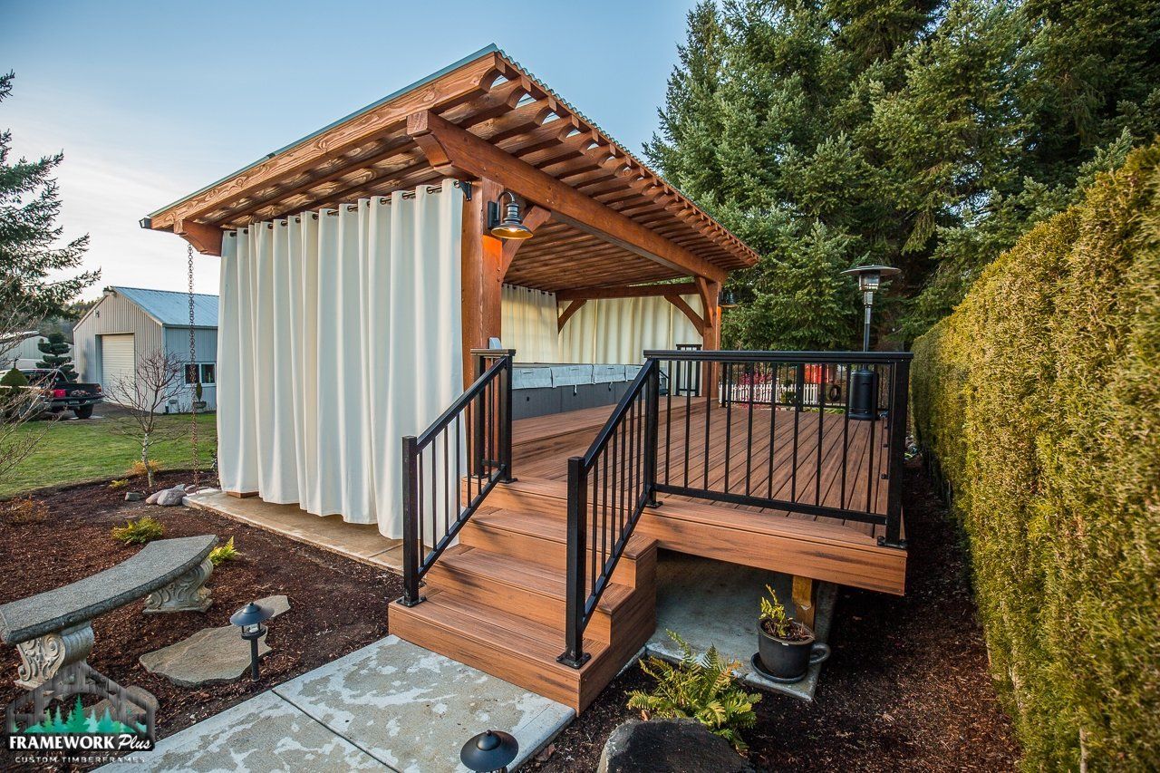 A wooden gazebo with white curtains and stairs leading to it.
