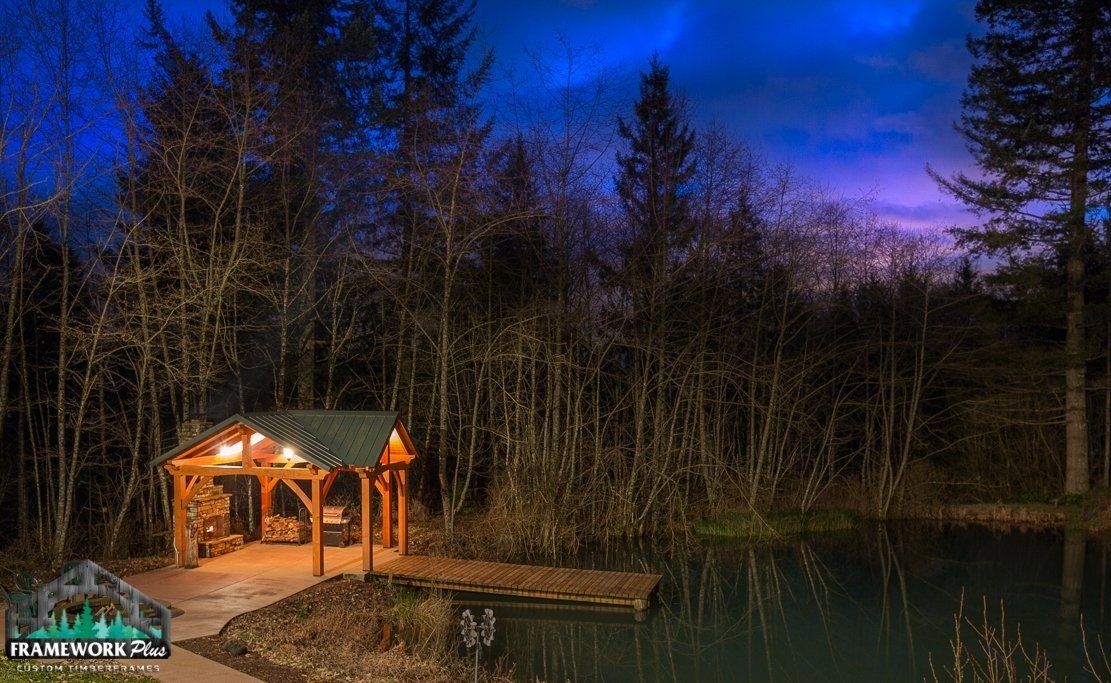 A log cabin is lit up at night in the middle of a forest next to a lake.