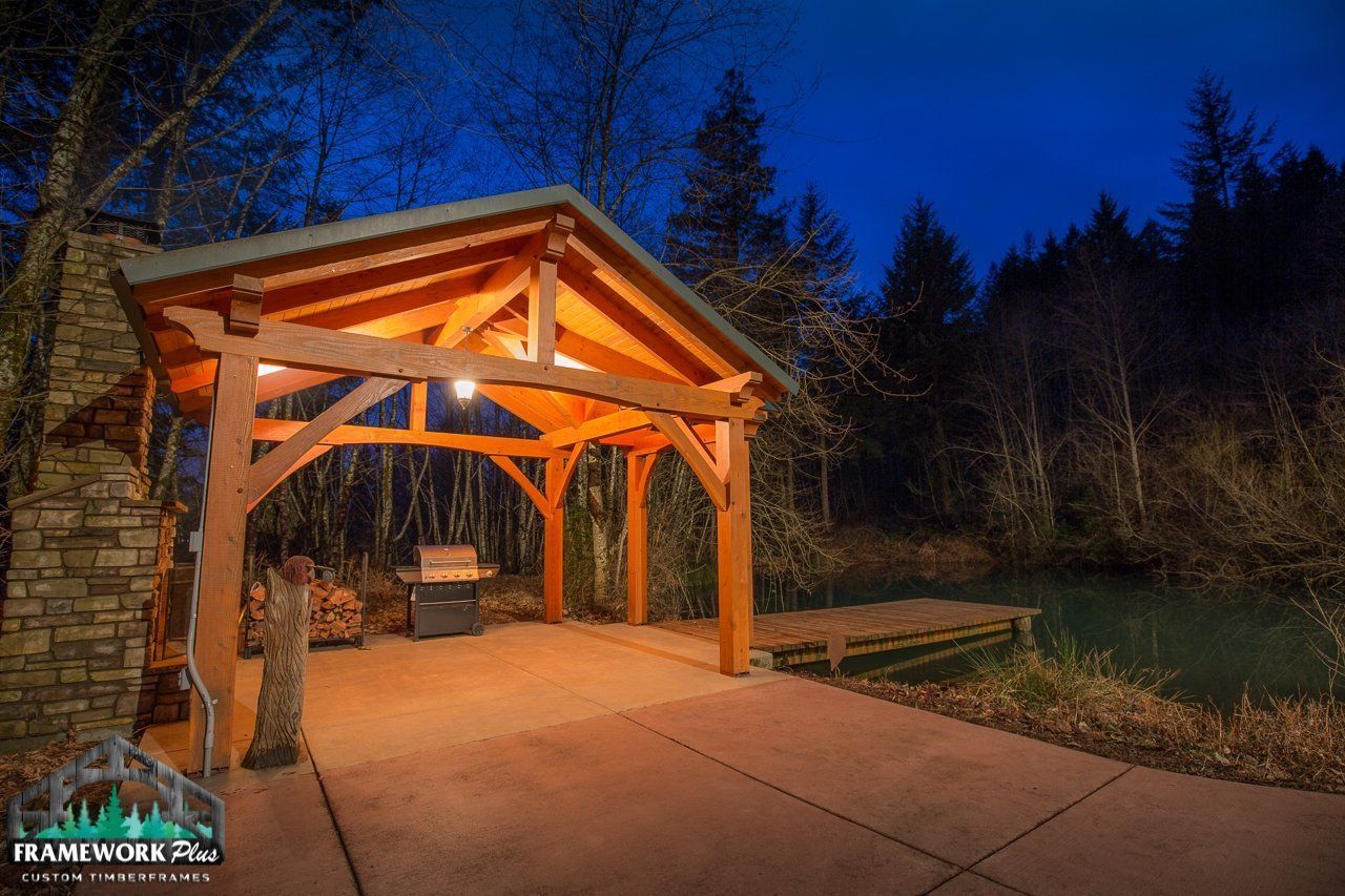 A wooden pavilion with a grill underneath it is lit up at night.