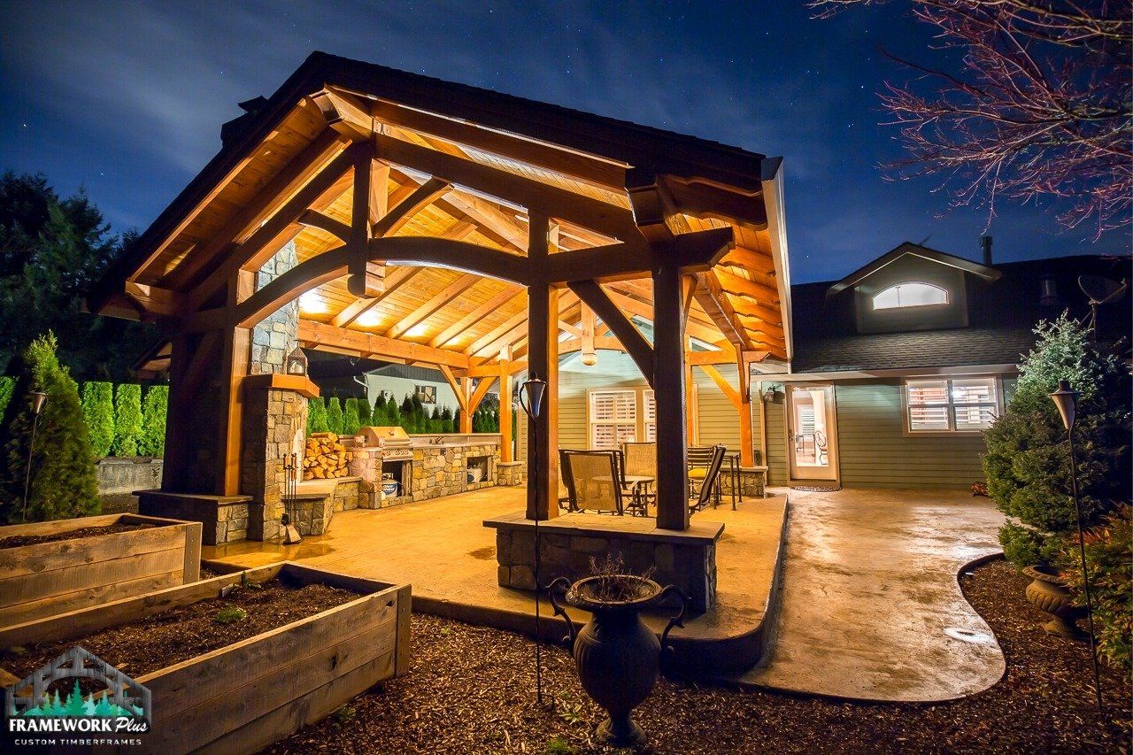 A large wooden pavilion is lit up at night in front of a house.