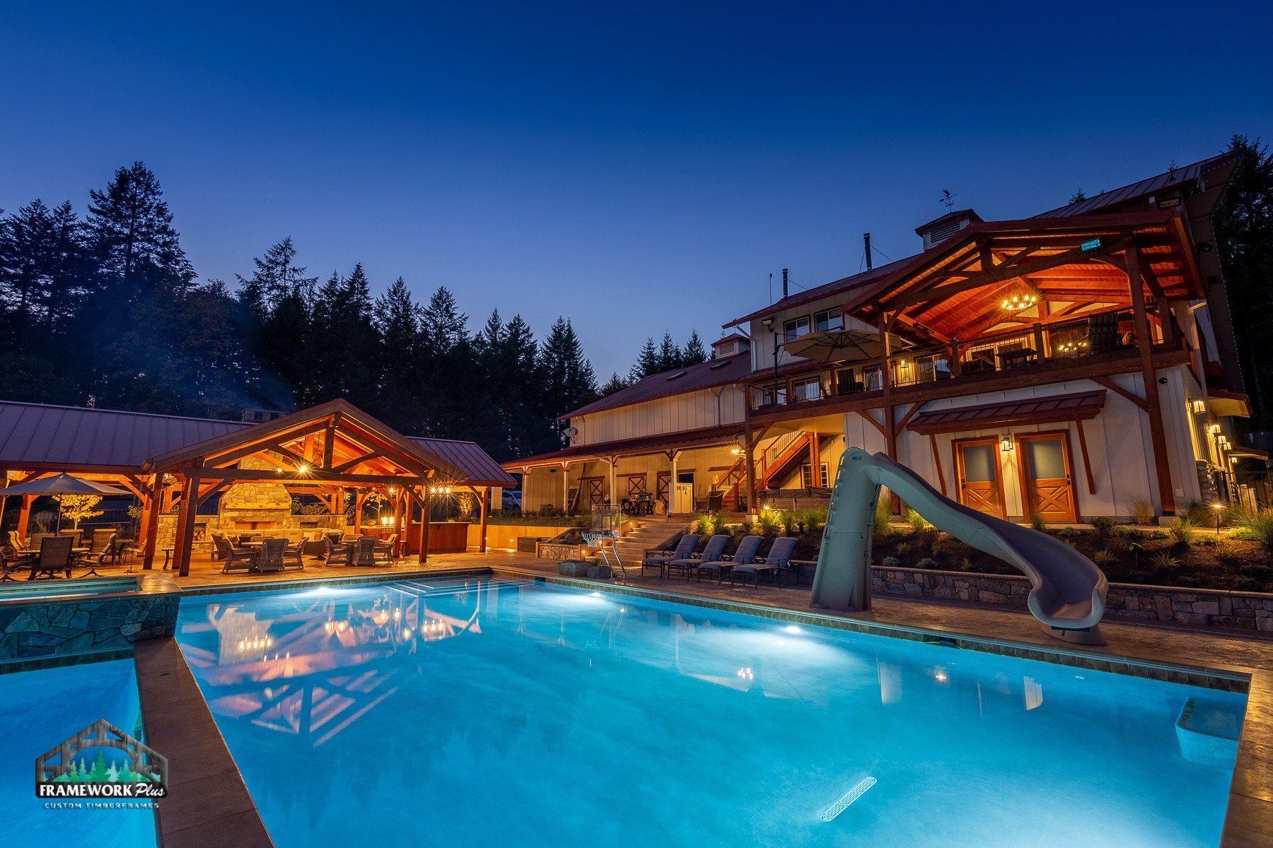 A large swimming pool is lit up at night in front of a large house.