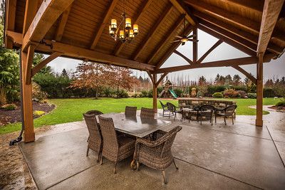 A wooden pavilion with a table and chairs underneath it in a backyard.