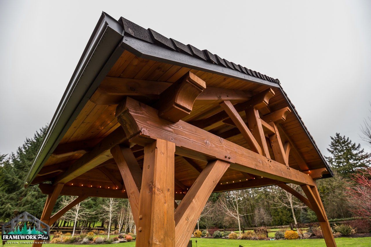 A wooden gazebo with a roof is sitting on top of a lush green field.