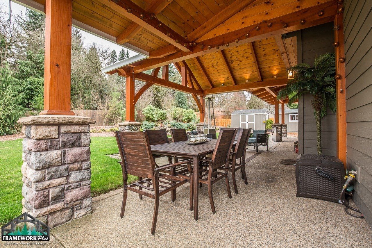A patio with a table and chairs under a wooden roof.