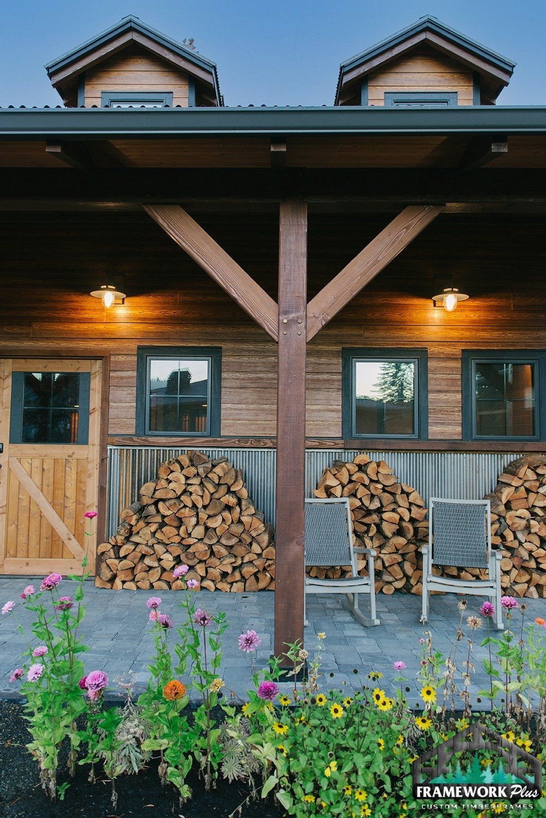 A wooden house with a covered porch and a pile of logs in front of it.