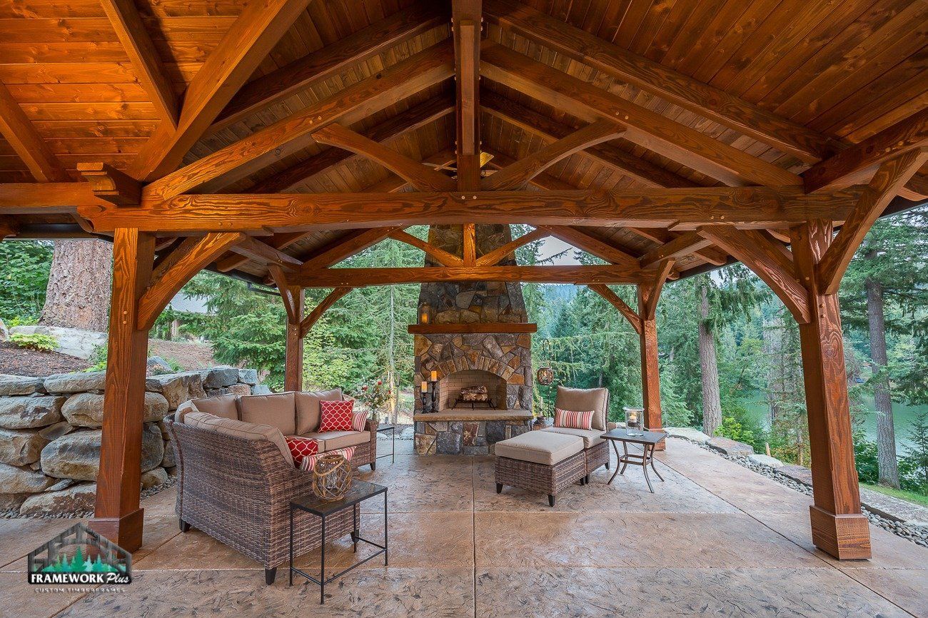A wooden gazebo with a fireplace and a couch underneath it.