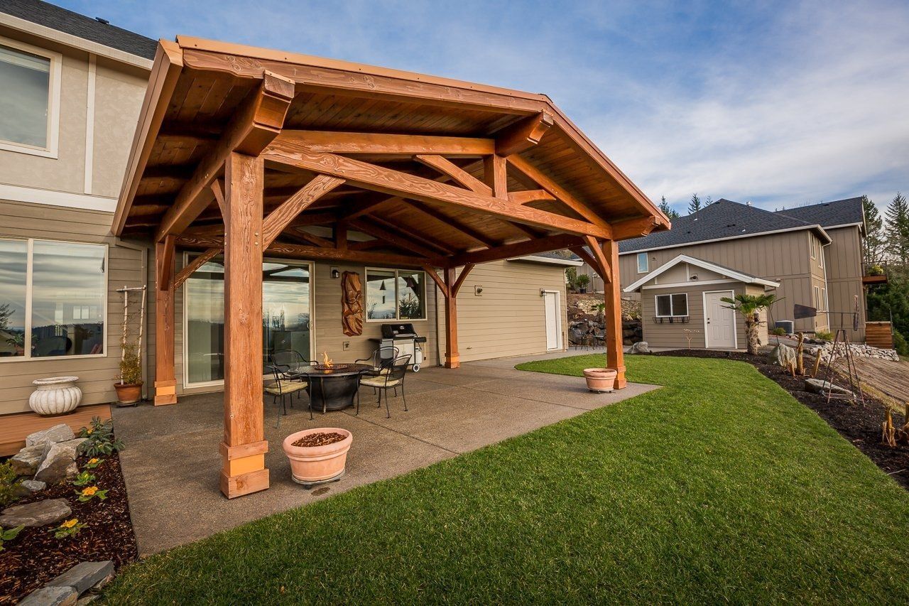 A large wooden pavilion is in the backyard of a house.