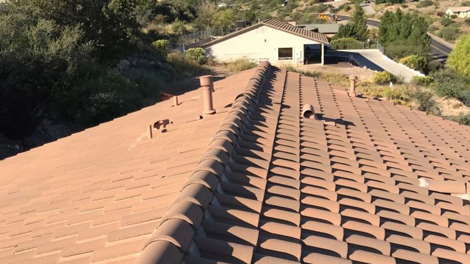 Brown tiled roof with vents, overlooking a hillside with a building.