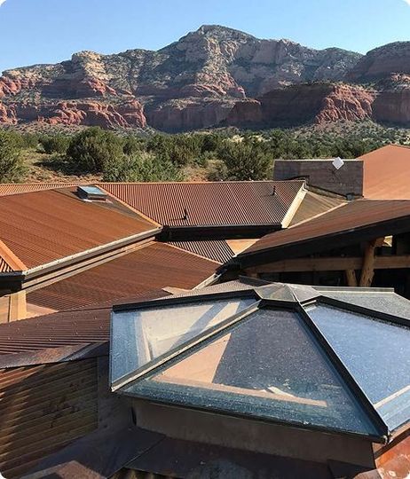 Rusty metal roofs with skylights against a backdrop of red rock mountains and a blue sky.