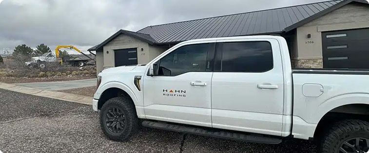 White pickup truck parked in front of a house under construction; a yellow excavator operates in the background.